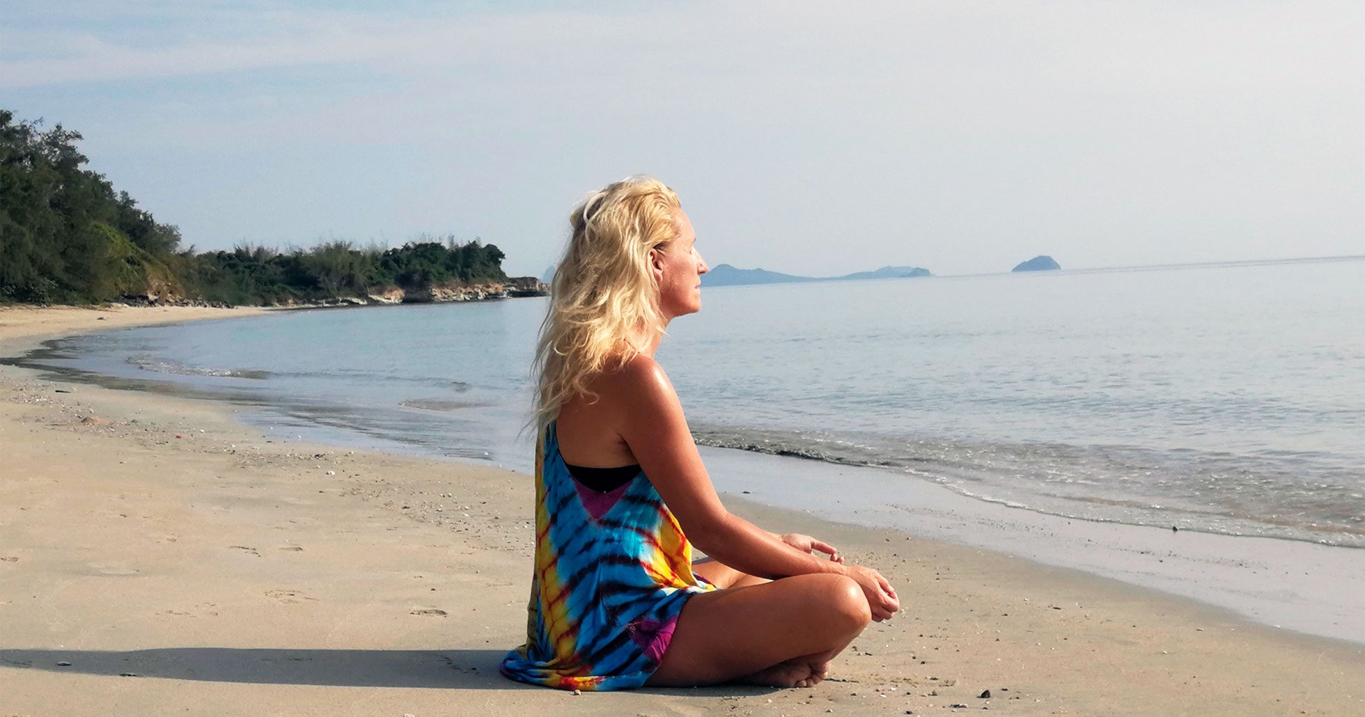 Anette sitter på en strand och utövar migränyoga.